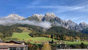 Alpenpanorama mit schneebedeckten Gipfeln, Nebel und grünen Wiesen in Österreich