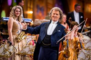 André Rieu spielt lächelnd Geige vor seinem Orchester auf der Konzertbühne