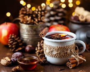 Becher Glühwein mit Zimtstange und Sternanis, weihnachtliche Deko im Hintergrund