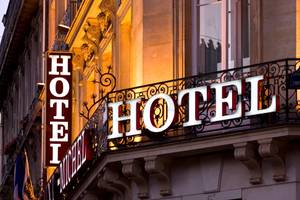Beleuchtetes Hotel-Schild an Fassade mit schmiedeeisernem Balkon in Paris
