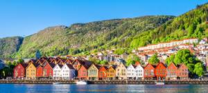 Bunte Bryggen-Häuser am Hafen von Bergen vor bewaldeten Bergen, Norwegen