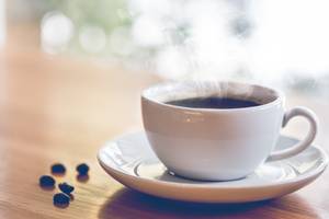 Dampfende Tasse frischer Kaffee mit Kaffeebohnen auf Holztisch im Café