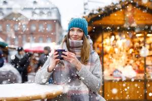 Frau trinkt heißen Punsch auf einem deutschen Weihnachtsmarkt.