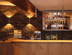 Gemütliche Hotelbar mit Steinwand, Holztresen und Weingläserregal im Schillingshof