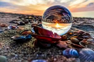 Glaskugel mit Sonnenuntergang-Spiegelung zwischen Muscheln am Ostseestrand