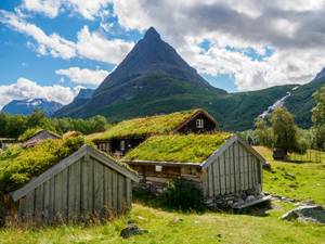 Grasdach-Holzhäuser in Innerdalen vor markantem Berggipfel, Norwegen