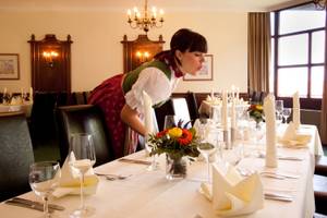Kellnerin in Tracht deckt festlich eingedeckten Tisch im Restaurant Hotel Schillingshof