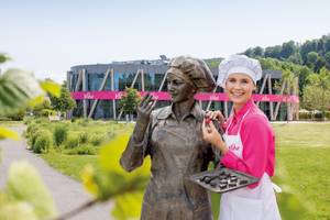 Konditorin in Pink neben Bronzestatue vor Viba-Firmengebäude im Grünen