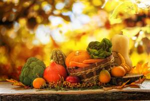 Korb mit Erntedank-Gemüse und Kürbissen vor herbstlichem Laubhintergrund