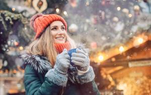 Lächelnde Frau mit Glühweintasse vor Weihnachtsbaum auf Weihnachtsmarkt im Schnee