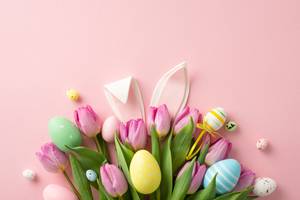 Osterdeko mit Hasenohren, bunten Ostereiern und rosa Tulpenstrauß