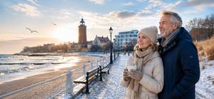 Paar mit Kaffee genießt Winterausblick auf Ostseestrand und Leuchtturm in Kolberg