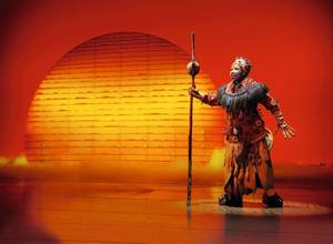 Rafiki-Darsteller mit Kostüm vor Sonnenkulisse bei König der Löwen Musical Hamburg
