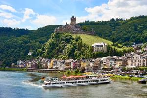 Reichsburg Cochem über der Mosel mit Flusskreuzfahrtschiff und bunter Altstadt