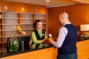 Rezeption Ahorn Hotel am Fichtelberg mit lächelnder Mitarbeiterin und Gast in Oberwiesenthal