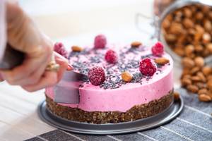 Rohkost-Torte mit rosa Guss, Himbeeren und Mandeln wird angeschnitten