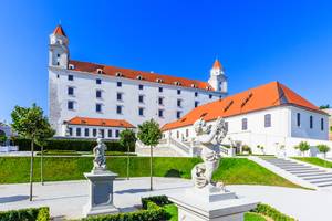 Schloss Bratislava mit barocken Statuen und Gartenanlage bei blauem Himmel