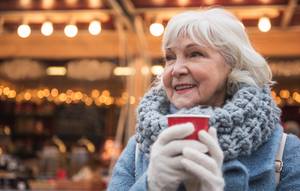 Seniorin mit Glühweinbecher lächelt auf Weihnachtsmarkt im Winter