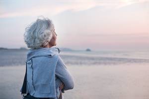 Seniorin mit grauem Haar blickt entspannt aufs Meer bei Sonnenuntergang