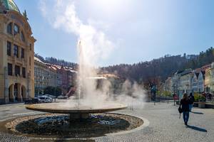 Sprudel-Geysir mit Dampf vor historischen Häusern in Karlsbad, Tschechien