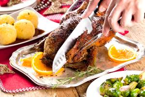 Weihnachtsgans wird tranchiert, serviert mit Kartoffelknödeln und Orangenscheiben