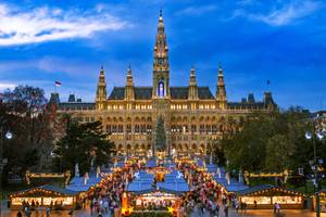 Wiener Rathaus mit beleuchtetem Weihnachtsmarkt und Christbaum bei Dämmerung