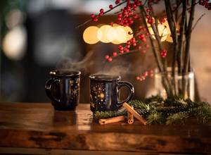 Zwei dampfende Tassen Glühwein mit Zimtstangen und Weihnachtsdekoration